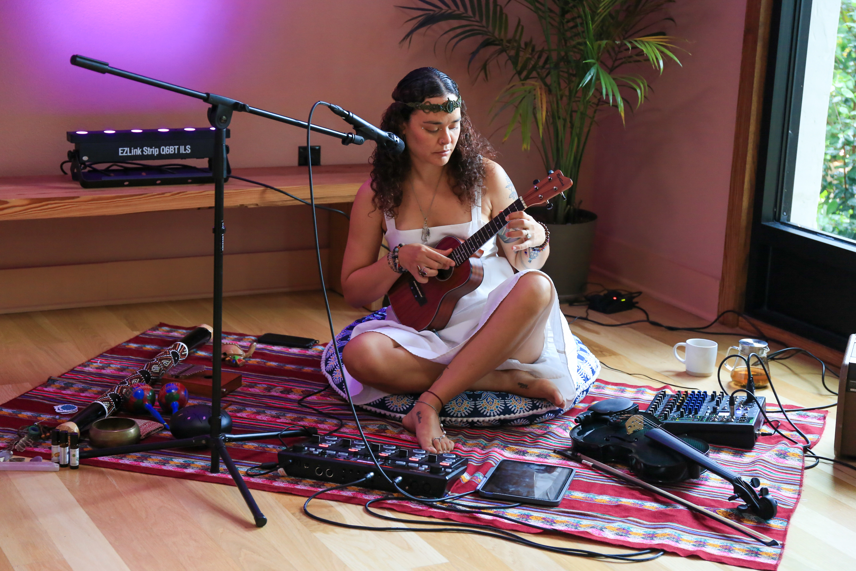Sisy Jamaraam seated among her instruments, playing ukulele during a live gathering.